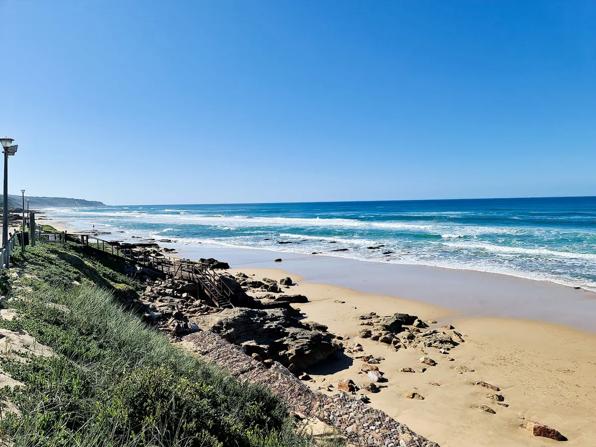 Long empty stretch of sand at Dana Bay with rock shelves in the shallows and a wooden stairway down