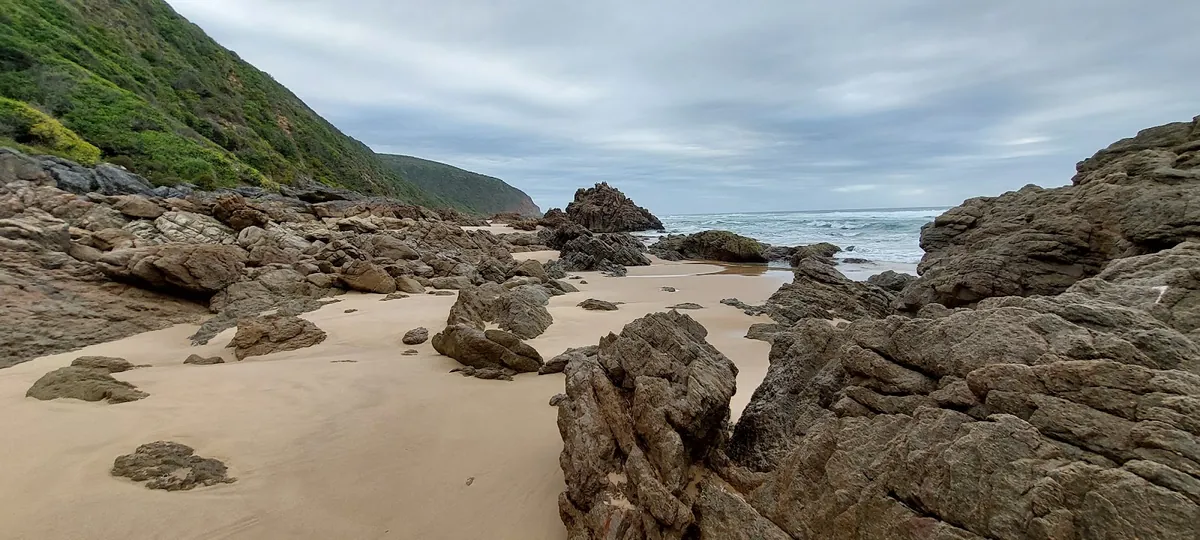 Sandstone boulders across wet sand at low tide on Glentana Beach, green headland rising on the left