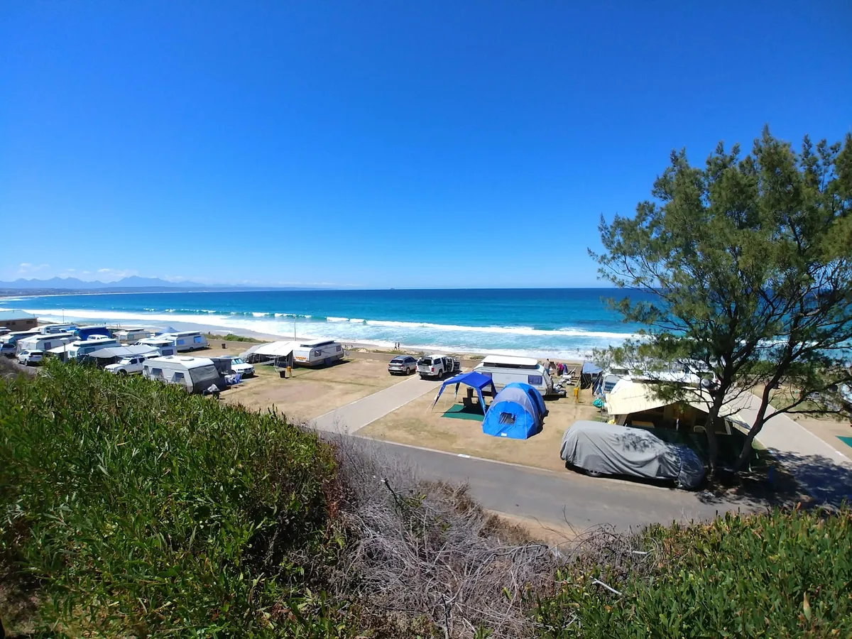 Caravans and tents on the grassy terrace above the long surf beach at Hartenbos, sea beyond