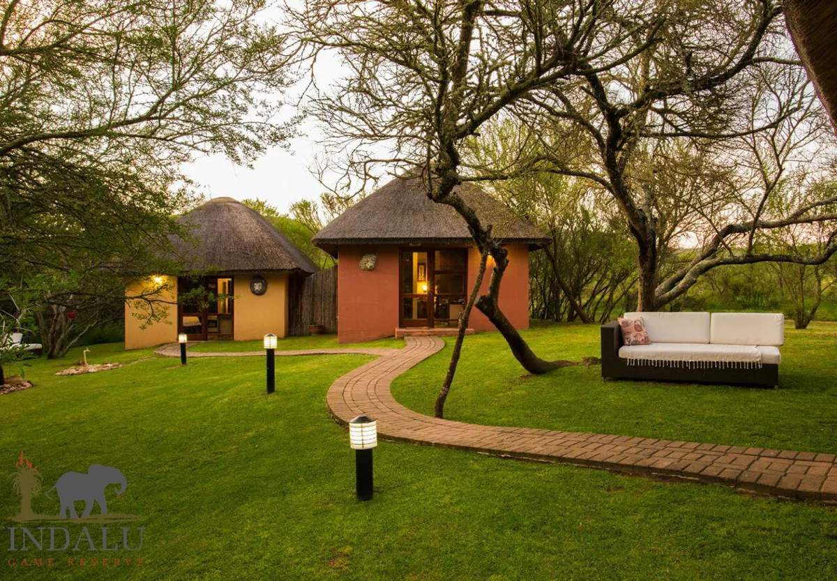 Two thatched rondavels on lawn at dusk at Indalu Game Reserve, with a brick path curving between acacia trees