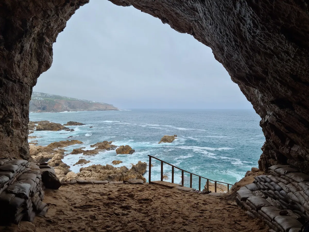 The view out of one of the Pinnacle Point caves near Mossel Bay, a guided walkway descending the cliff to the rocky shore below