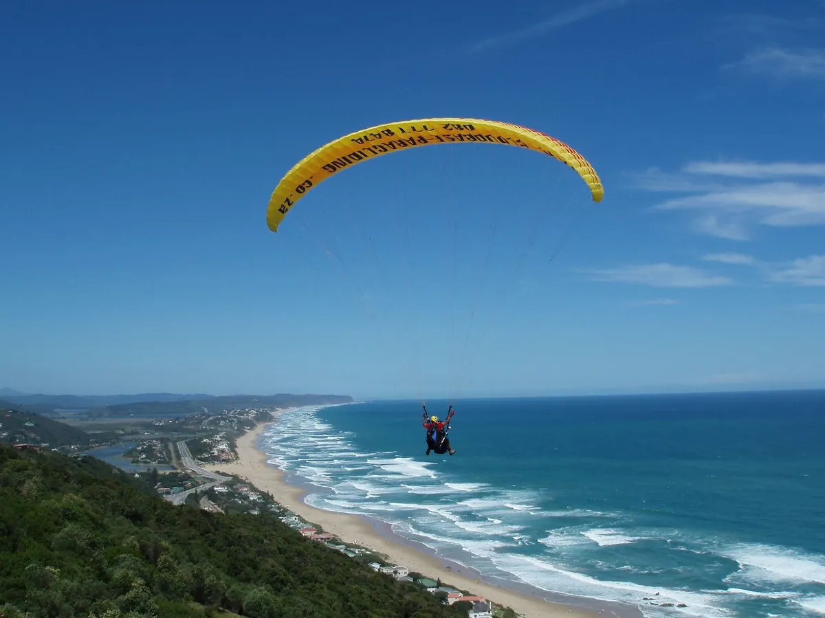 Tandem paraglider under a yellow wing above Wilderness beach and lagoon
