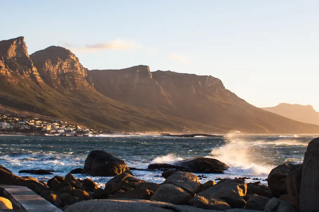 Late sun on the Twelve Apostles, with waves breaking over granite boulders in the foreground and houses along the shore