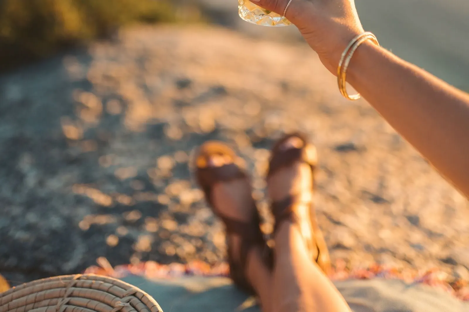 A hand holding a mojito with a slice of lime at sunset, with a blurred rocky coast behind